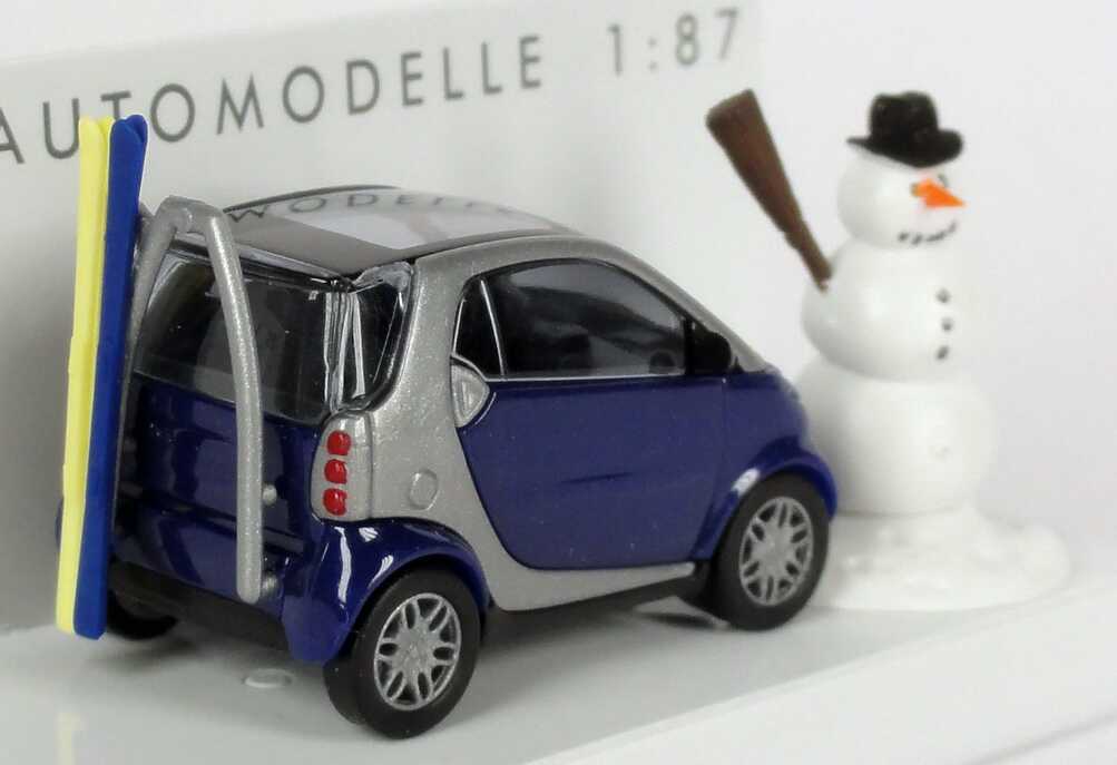 Foto 1:87 MCC Smart City-Coupé dunkelblau/silber mit Skiträger, Ski und Schneemann Busch 48918