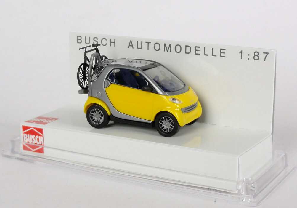 Foto 1:87 MCC Smart City-Coupé gelb/silber mit Fahrradträger und Fahrrad Busch 48907